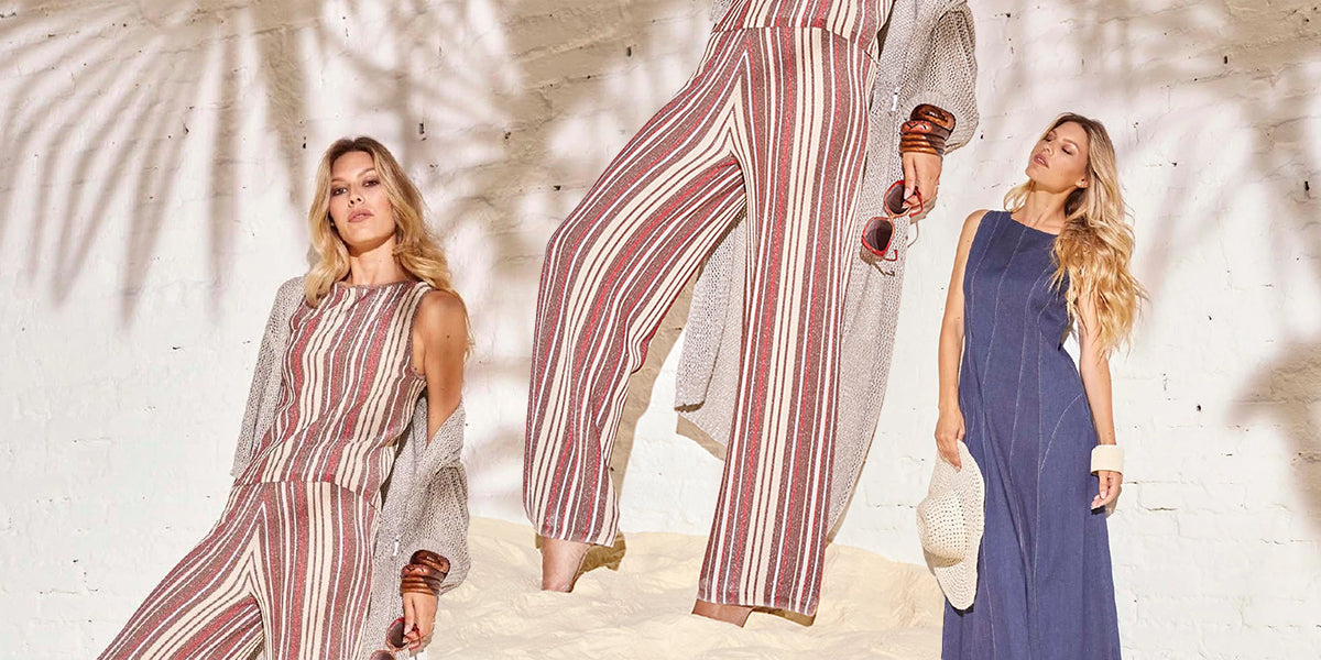 Modella con completo a righe verticali rosse e beige in lurex, e modella con abito jeans lungo con cuciture a vista